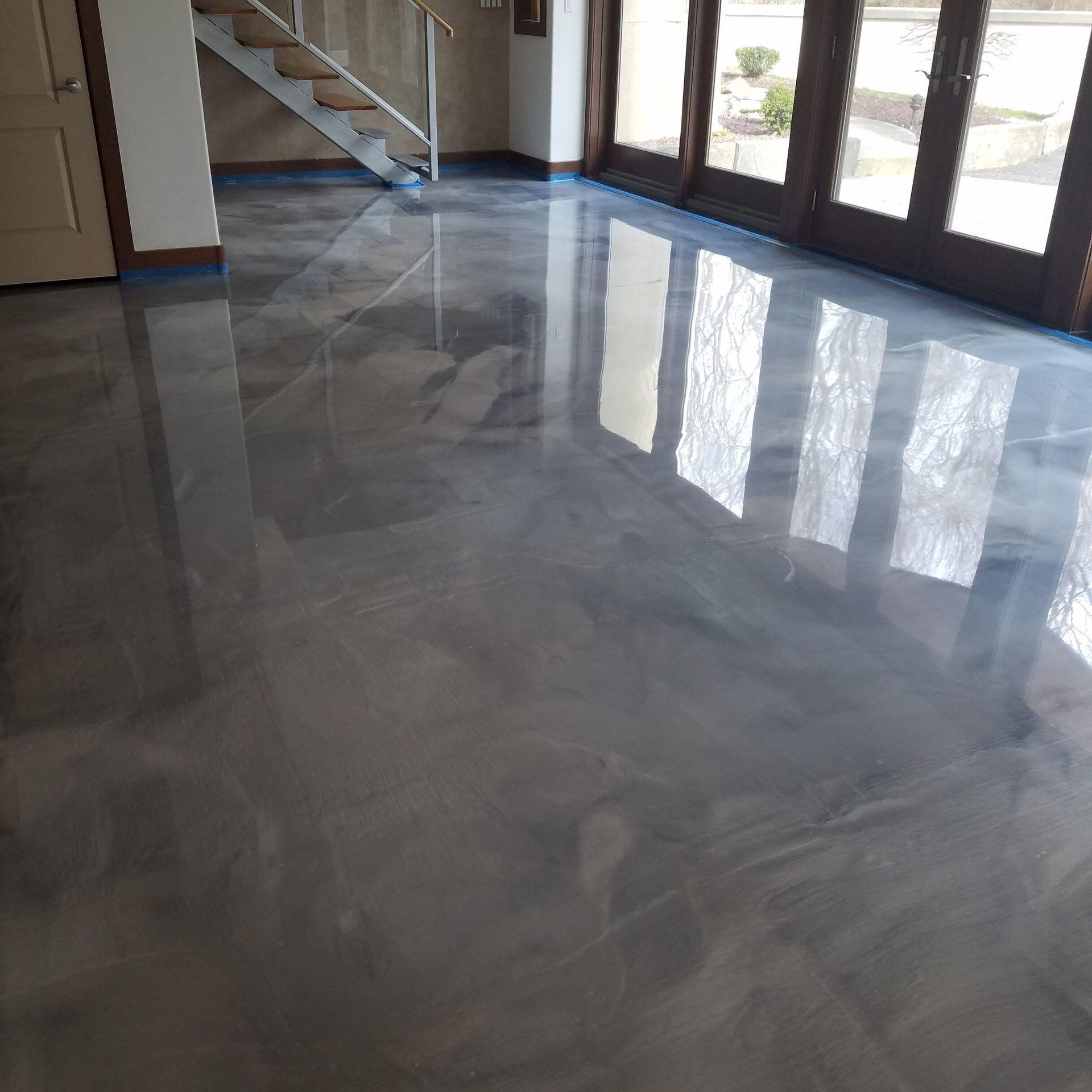 Polished concrete floor with reflections in a room with stairs and large windows.